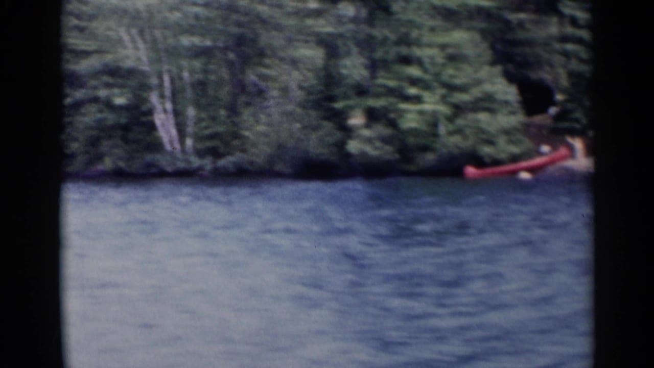Red canoe at the right edge of a forested shoreline across the lake.