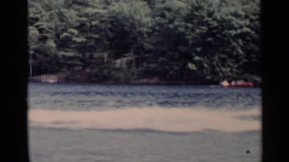 A red canoe appears near the far wooded bank of Lake George, with rippled water filling the foreground.