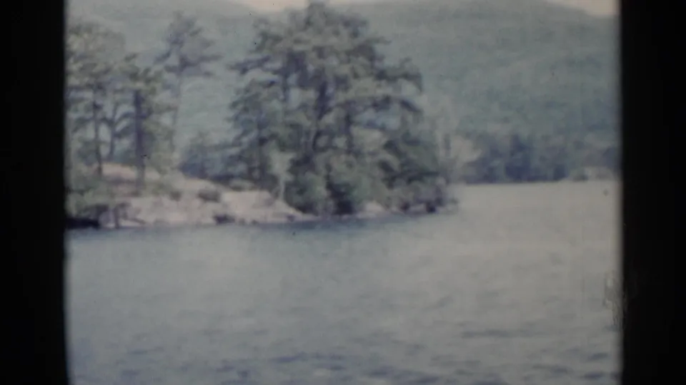 A small wooded island and rocky bank pass close to the camera during the 1955 Lake George boating footage.