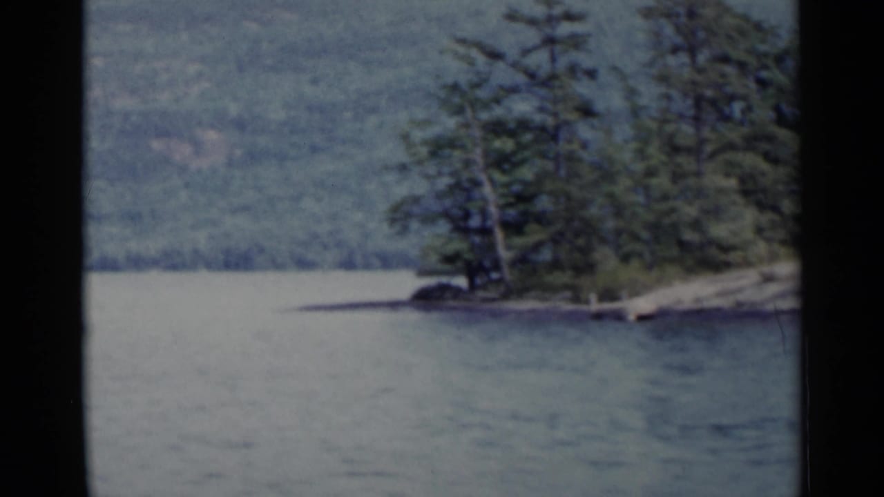 Tree-covered point extends into lake water with forested hills in the distance.