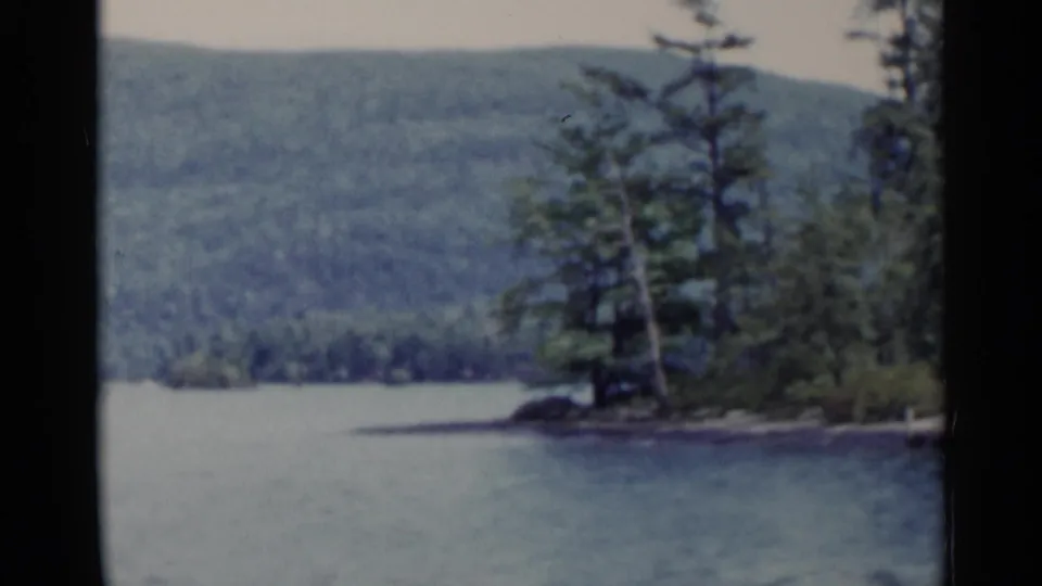 1955 Lake George frame of calm water, a wooded point, rocky shore, and forested Adirondack hills in the background.