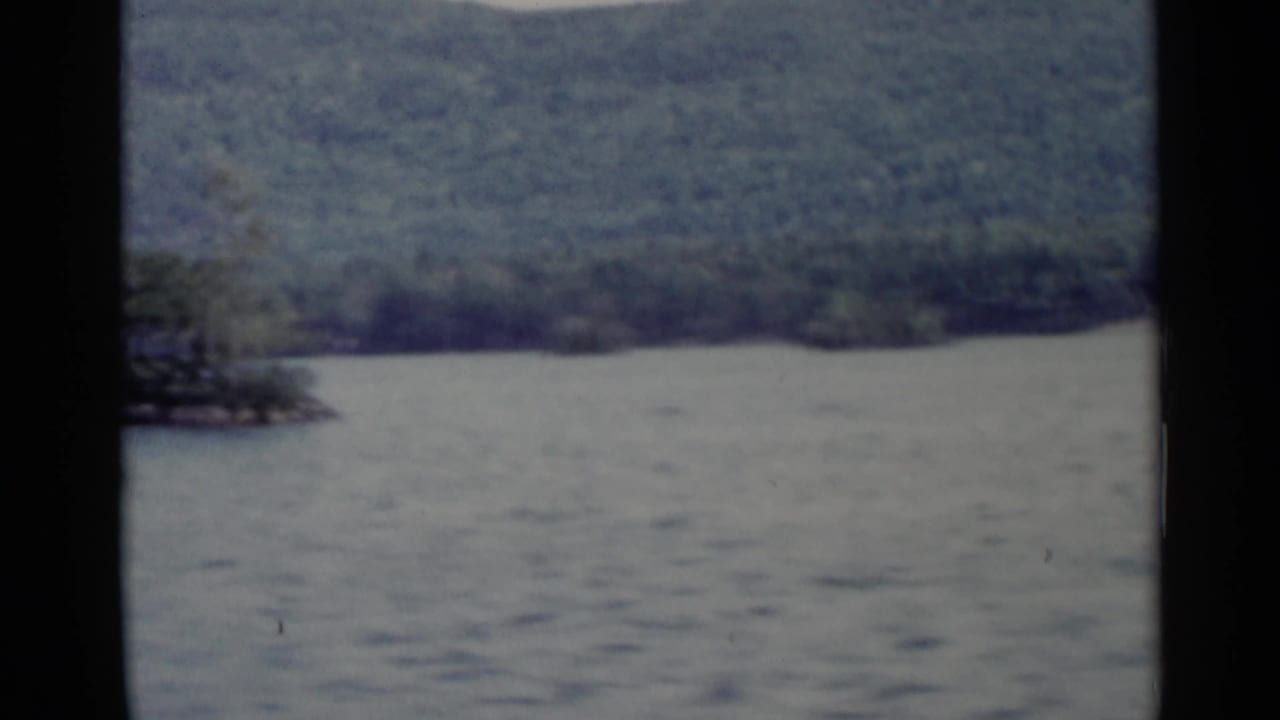 Lake water and wooded hills seen through a dark vehicle window frame.