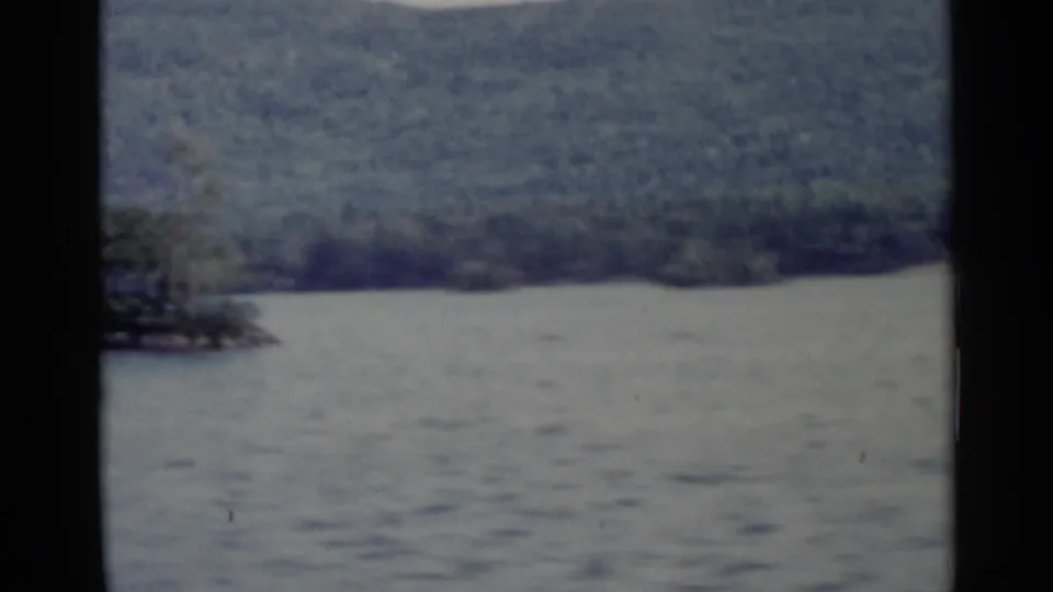1955 Lake George scenery with calm water, distant forested hills, and a dark window frame crossing the view.