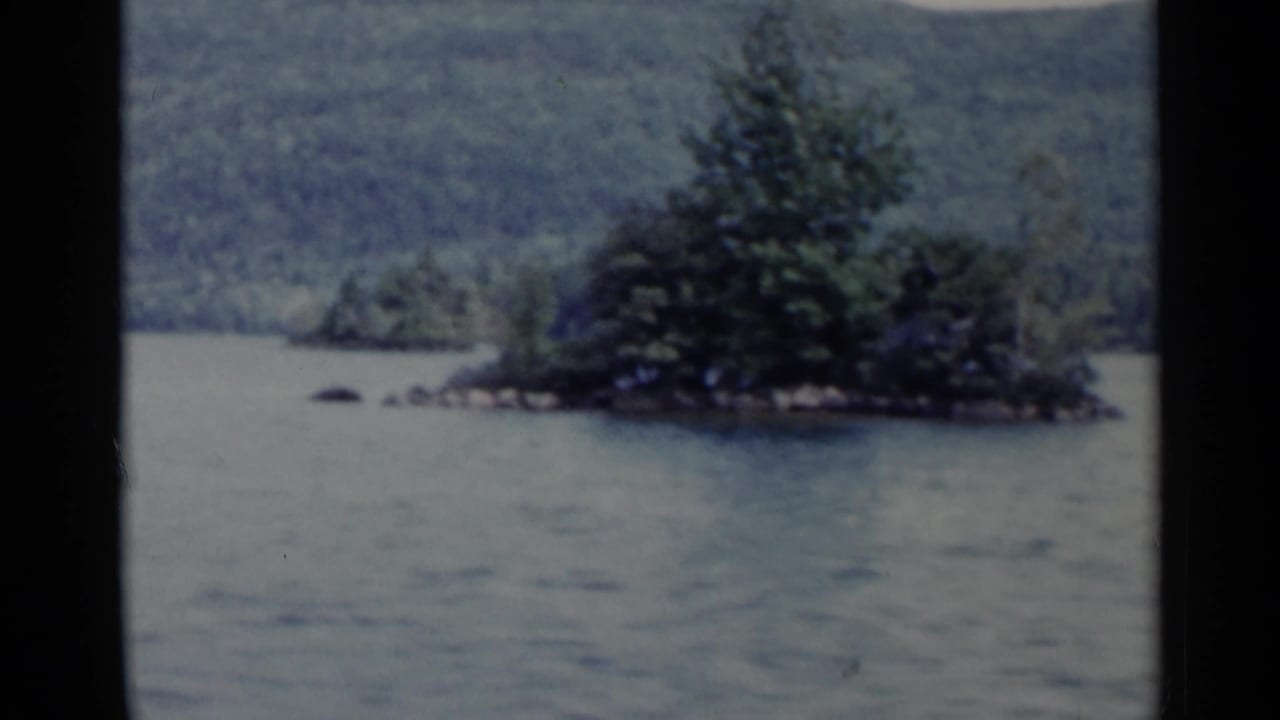 Tree-covered island on a lake with wooded hills behind it.