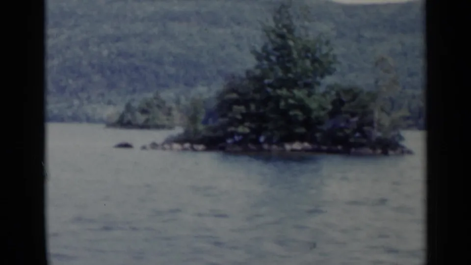 Lake George view showing a small tree-covered island, open water, distant hills, and a dark window divider.
