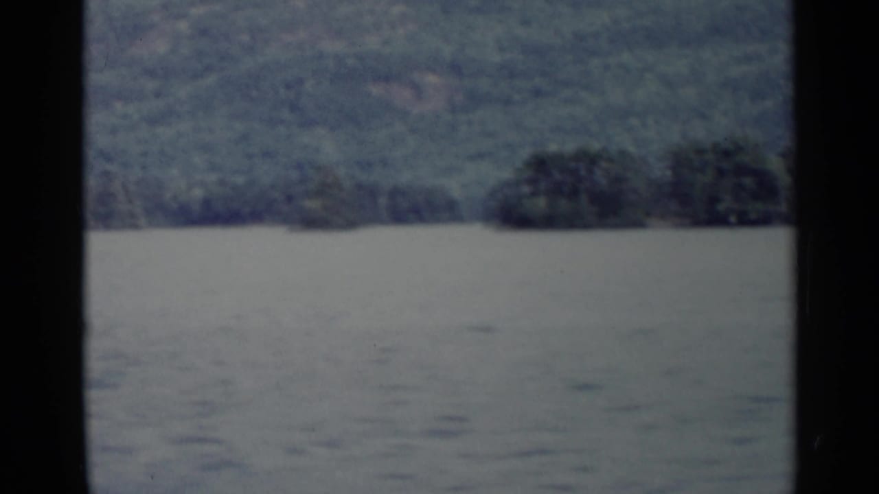 Wide 1955 Lake George view with muted water, distant wooded shoreline, and soft 8mm exposure.