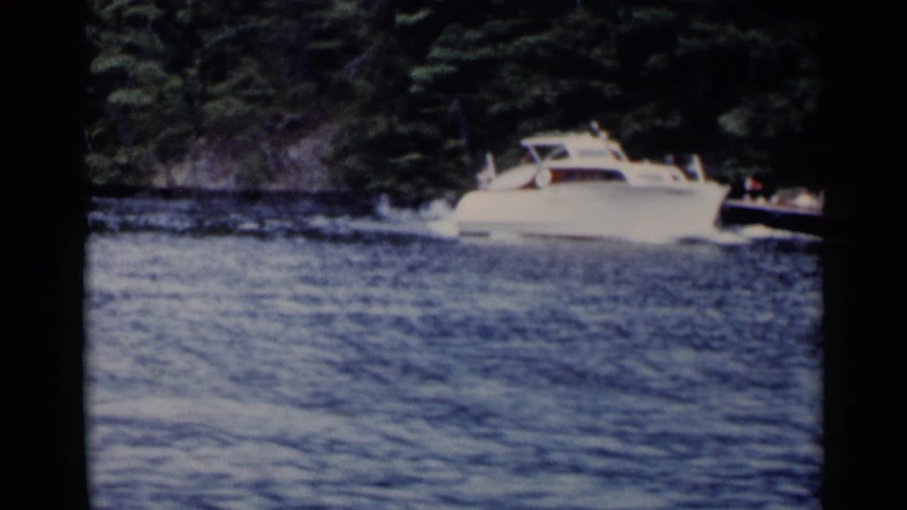 White cabin speedboat moving across a lake near a wooded shoreline.