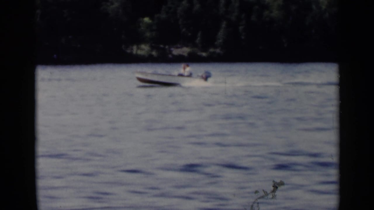 Small outboard motorboat crossing open lake water with a person aboard.