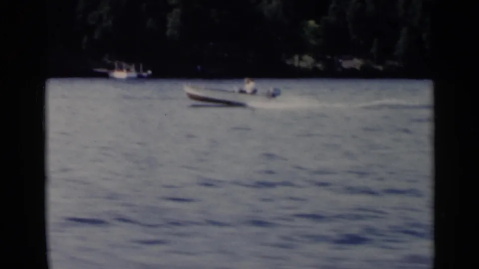 Lake George frame with a small motorboat in the distance and another boat near the wooded shore.