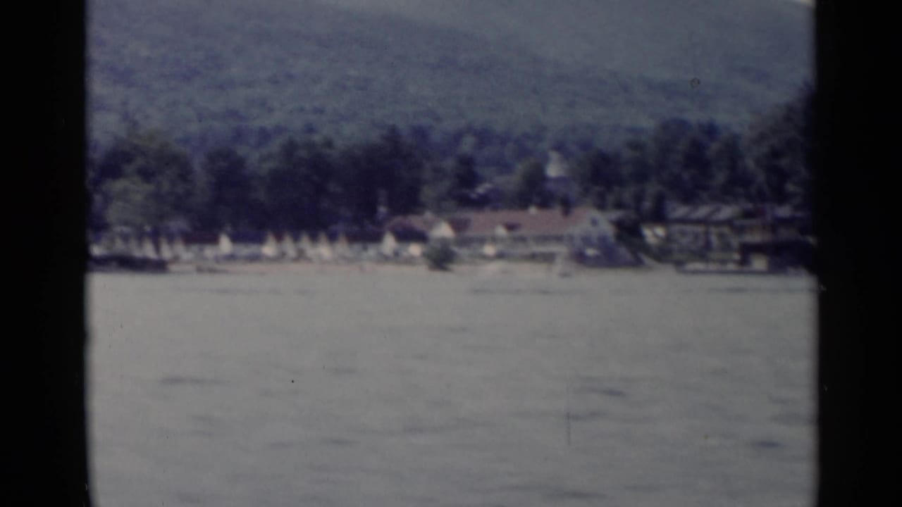 Wide lake view with shoreline buildings, trees, and mountains.
