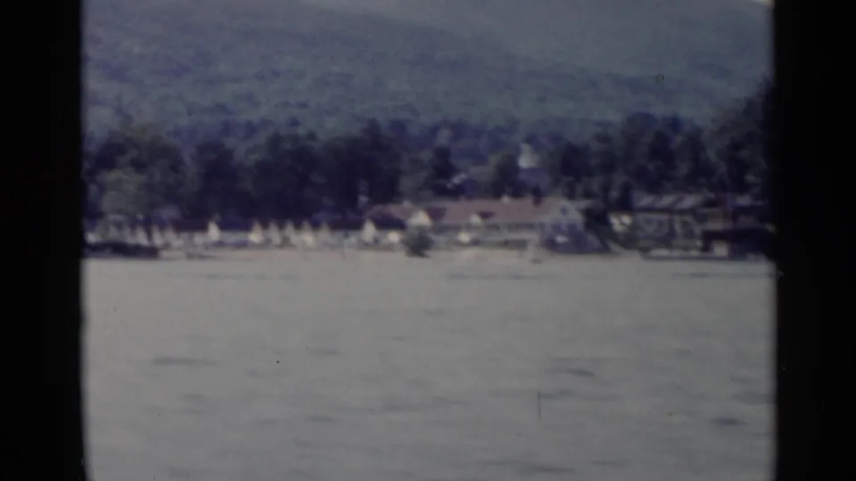 Lake George shoreline appears across the water, with trees, small buildings, and mountain slopes in the background.