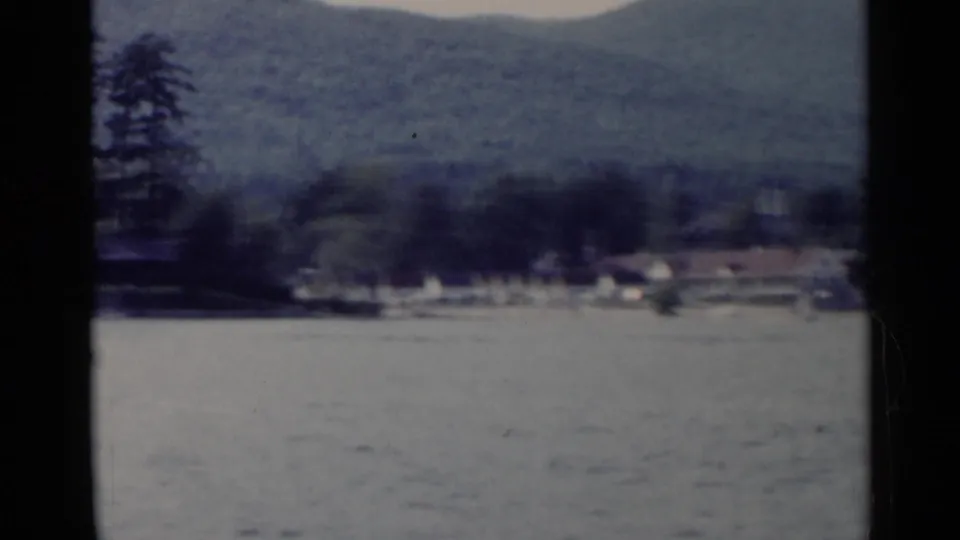 A soft 8mm frame shows Lake George water in the foreground and a wooded mountain shoreline beyond.