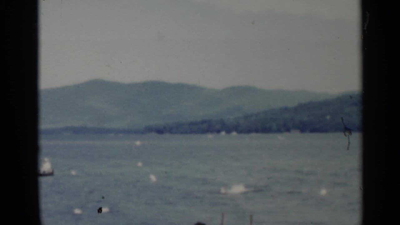 Lake surface with distant shoreline, hills, small boat shapes, and dark frame borders.