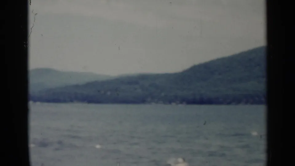 Soft 8mm Lake George view of water and a wooded hillside, with the scene framed by dark scan borders and muted color.