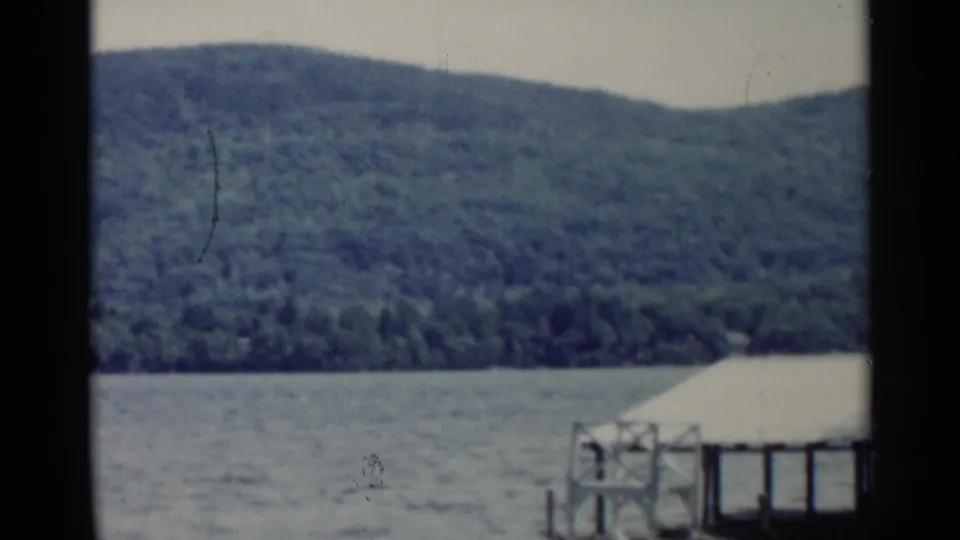 1955 Lake George view with water and forested hills, plus a partial lakeside dock or covered structure at the lower right edge.