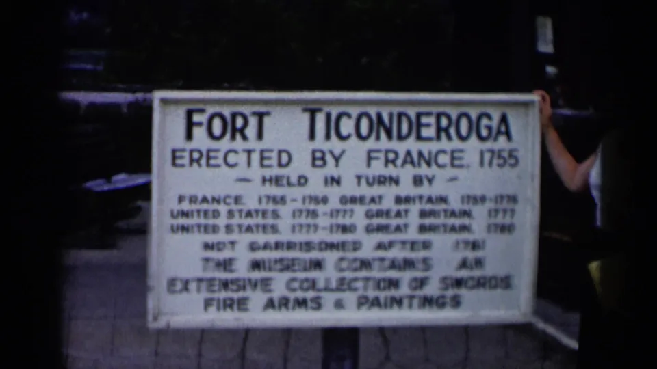 A closer 8mm view shows the Fort Ticonderoga sign describing its French origin and museum collection, with a visitor partly cut off.