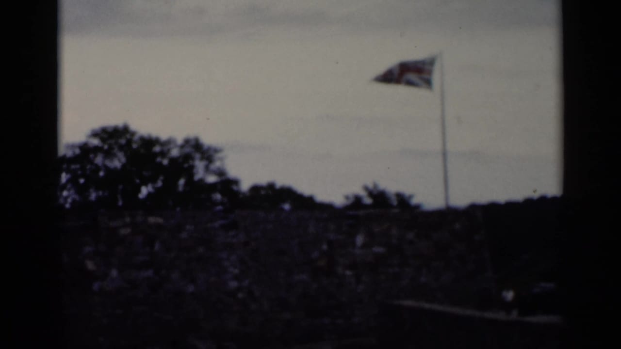 Stone wall and flagpole with a flag waving above trees under a cloudy sky.