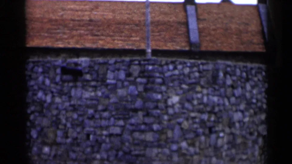 Close 1955 Lake George view of textured stonework, small wall openings, roof tiles, and vertical dark frame edges.