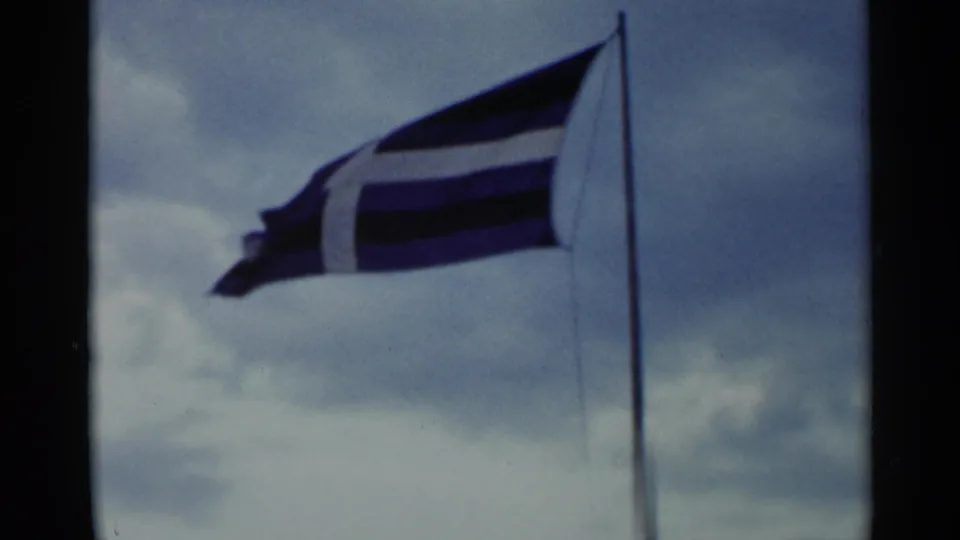 Close 1955 Lake George view of a blue-and-white striped flag waving on a pole against clouds.