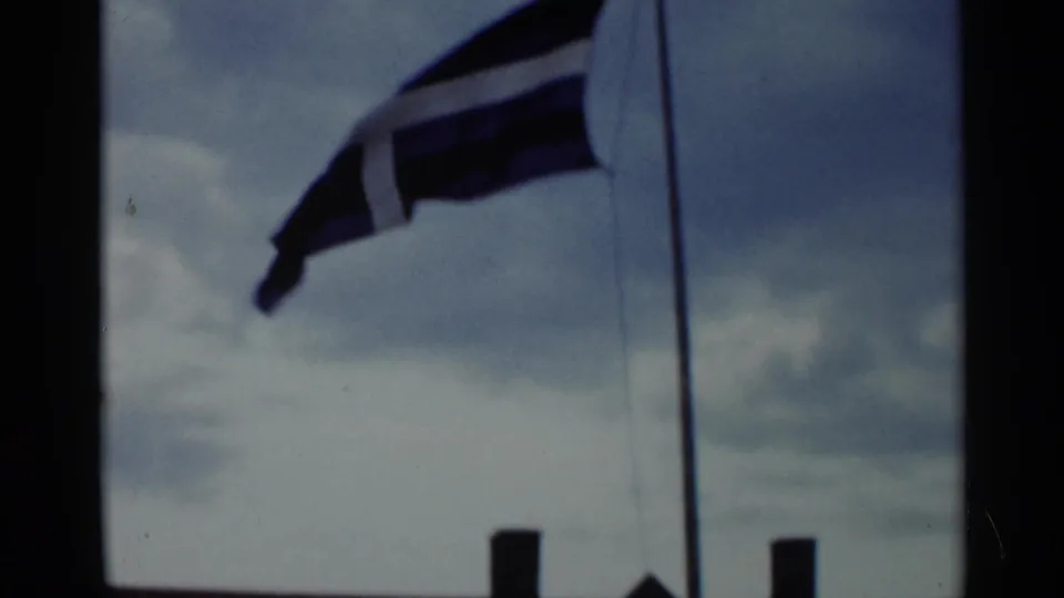 Home-movie frame from Lake George showing a striped flag in wind, cropped close against a cloudy sky.