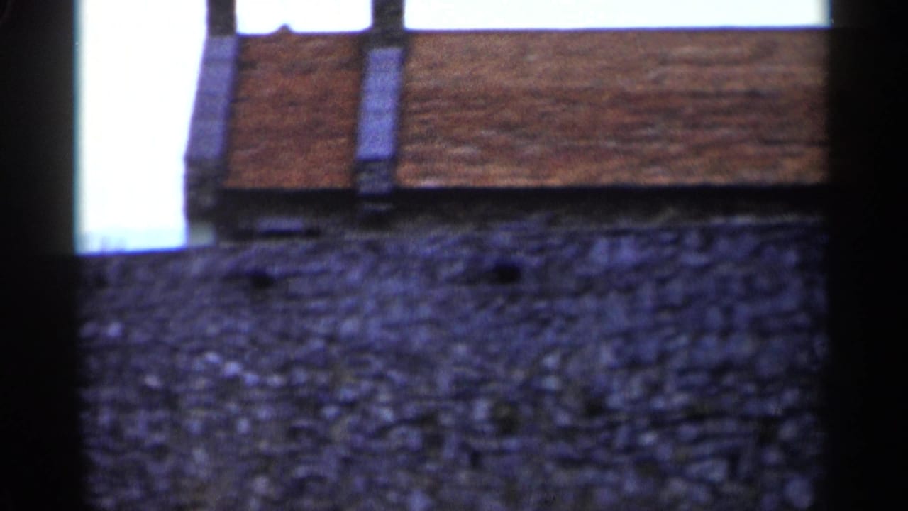 Rough stone wall below part of a brick building with dark film-frame edges.