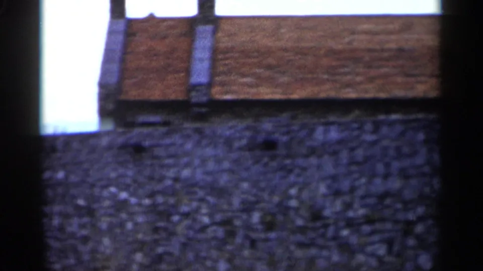 1955 Lake George home-movie frame showing a rough stone wall and brick building edge at a historic site.