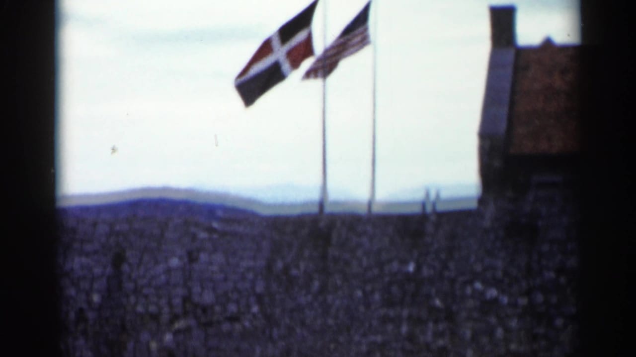 Flags fly above a rough stone wall at a Lake George historic site, with hills visible in the distance.