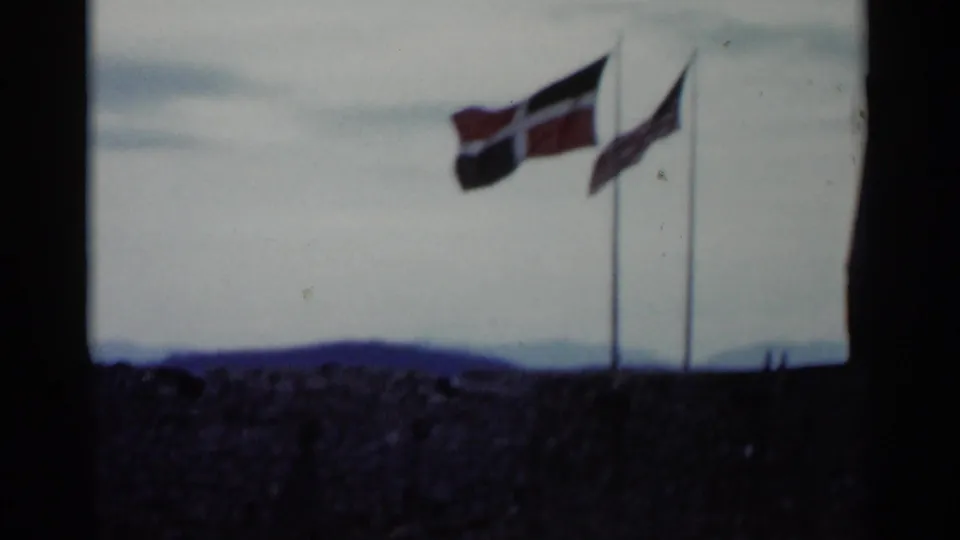 Norwegian and American flags appear to fly above a stone wall in 1955 Lake George travel footage.