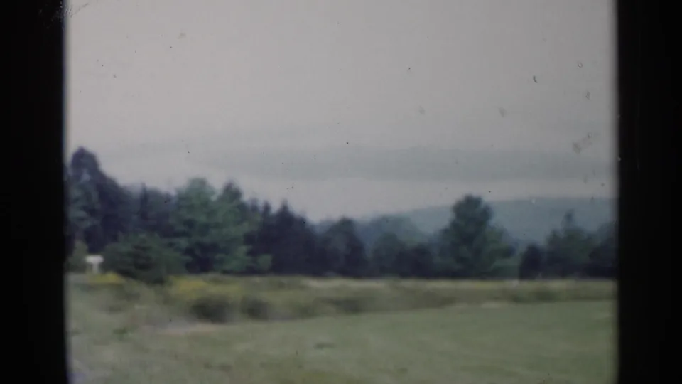 Soft 8mm Lake George landscape frame with field, treeline, and distant hills beneath an overcast sky.