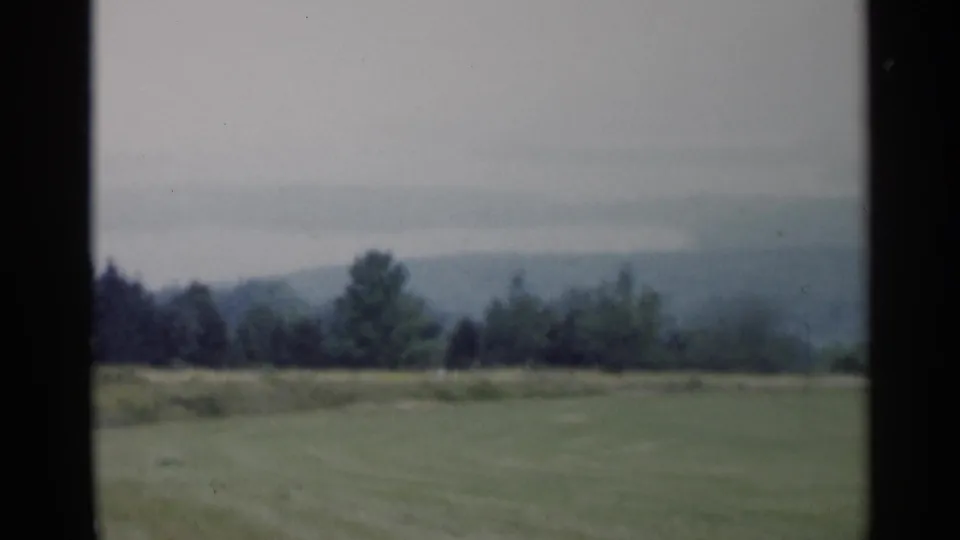 1955 Lake George scenic cutaway showing open grass, trees, and layered hazy hills in vintage 8mm color.