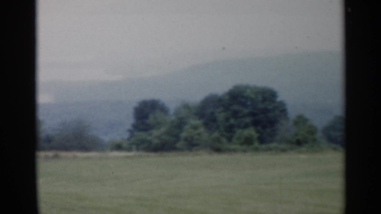 Lake George, New York countryside in 1955, showing open grass, dense trees, and misty wooded hills beyond.