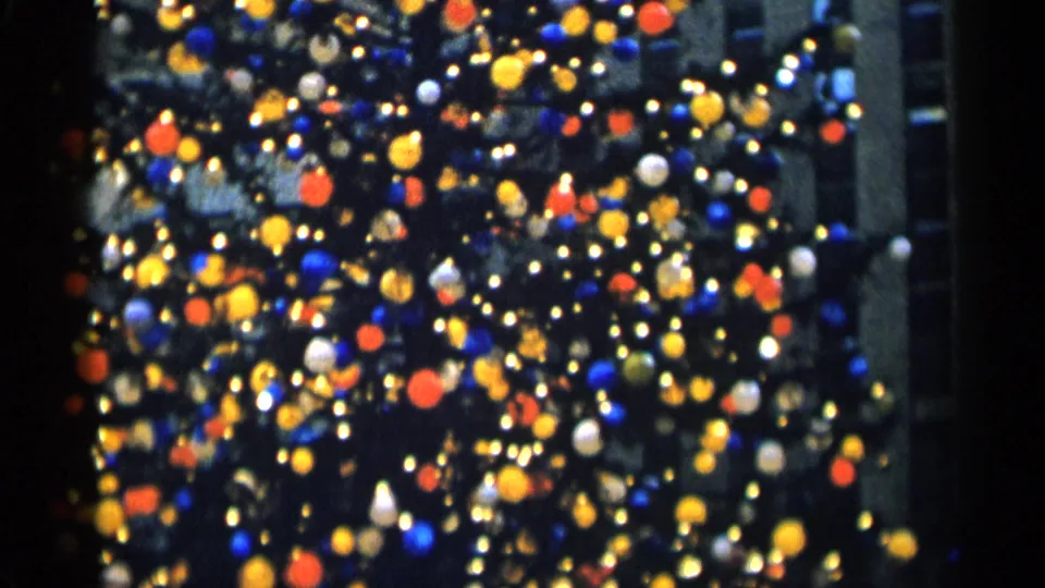 Out-of-focus 8mm view of a decorated Christmas tree in New York City, with colored lights and a vertical building edge visible.