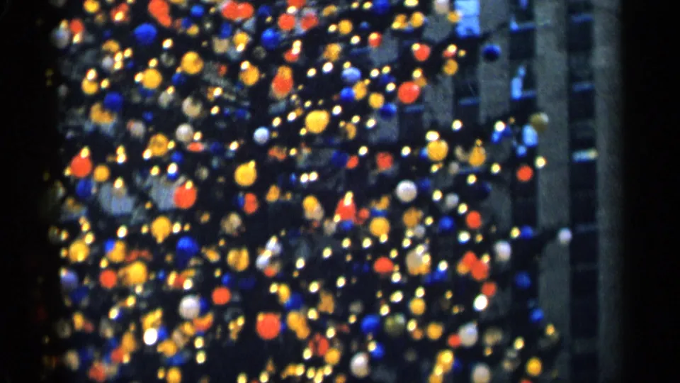 1955 8mm home-movie frame of a large Christmas tree, its lights and ornaments softened into dense festive bokeh.