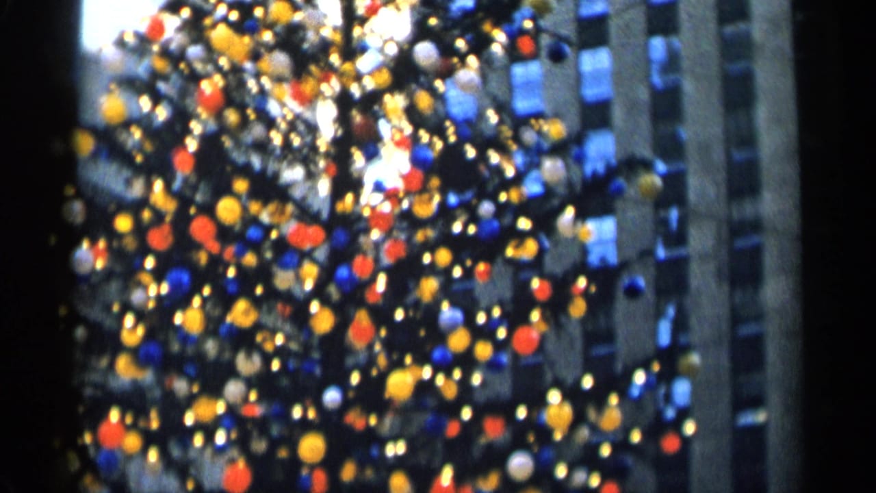 Soft-focus decorated Christmas tree with colorful ornaments in front of tall city buildings.