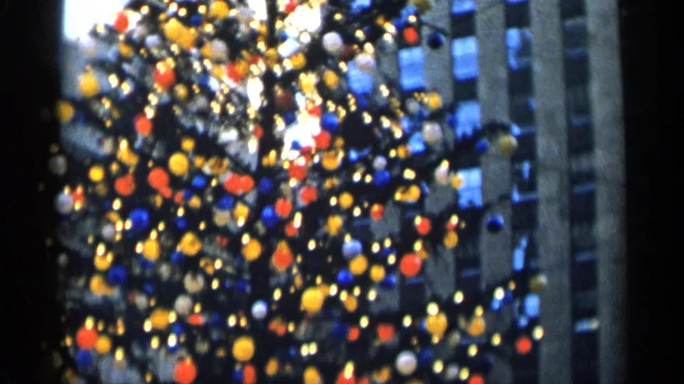 Soft 8mm view of a decorated Christmas tree in New York City, with colorful ornaments and lights against tall building facades.