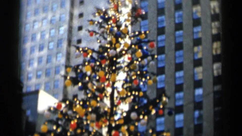 Wider soft-focus view of the decorated Christmas tree, with colorful ornaments and lights set among New York City high-rises.