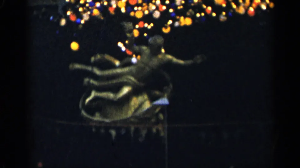 A golden sculpture, possibly a flying figure, sits beneath colored lights in the 1955 New York City night footage.