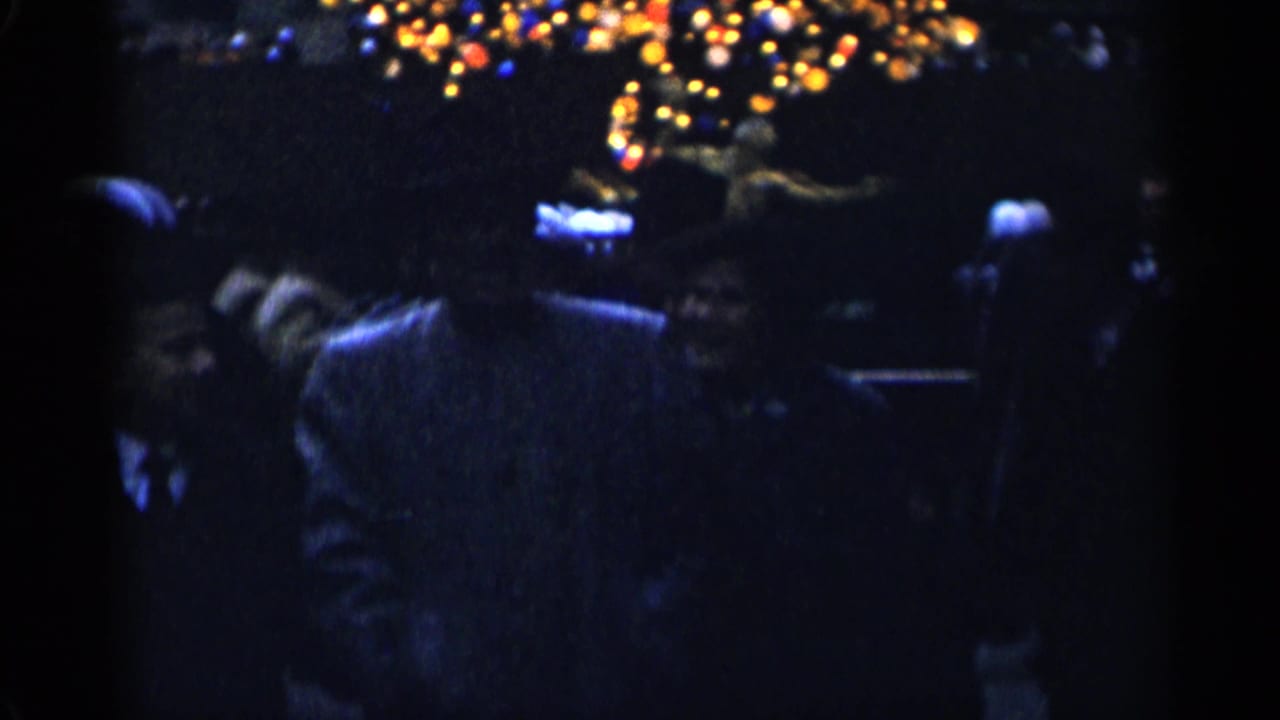 Pedestrians in dark winter clothing walk under blurred Christmas lights at night.