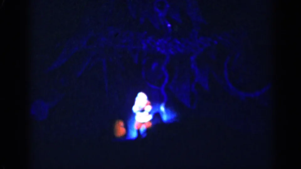 Nighttime 8mm frame with a small bright Santa-like holiday figure glowing in blue darkness, likely part of a Christmas display.