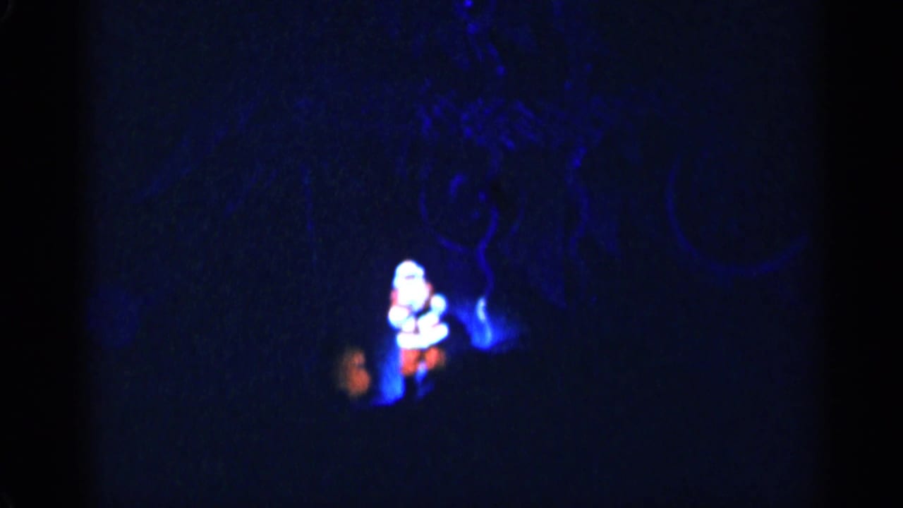 Distant Santa figure on a dark blue stage with a painted backdrop.