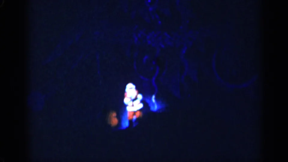 1955 New York City 8mm frame showing a distant Santa figure under blue stage light during a Christmas performance.
