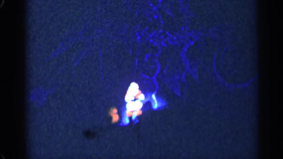 Distant 8mm frame from the New York City Christmas performance showing Santa and a small orange-lit figure on stage.