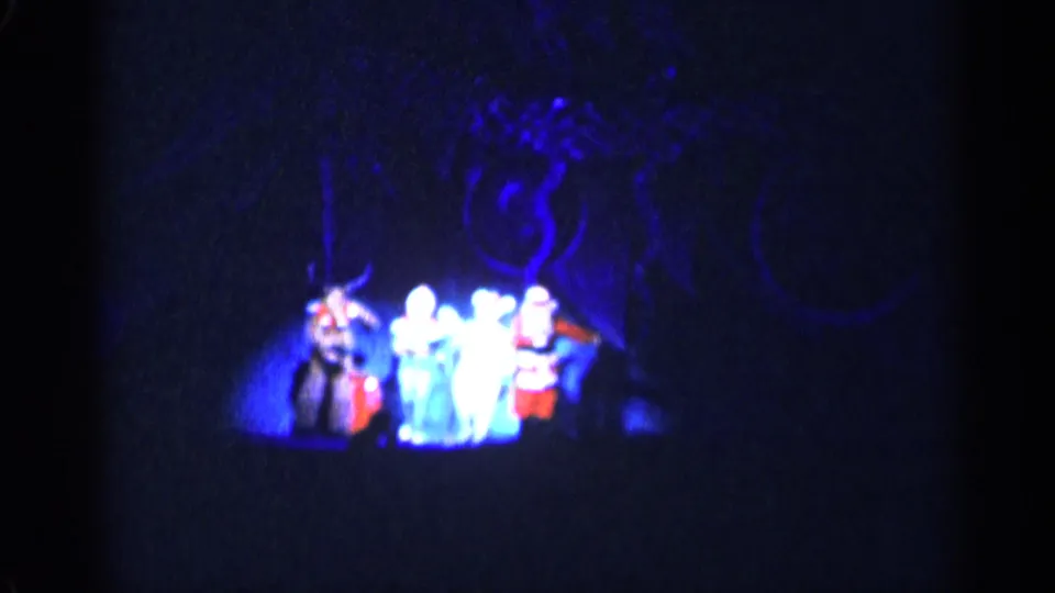 1955 New York City home-movie frame showing Santa and several costumed performers grouped on a blue-lit stage.