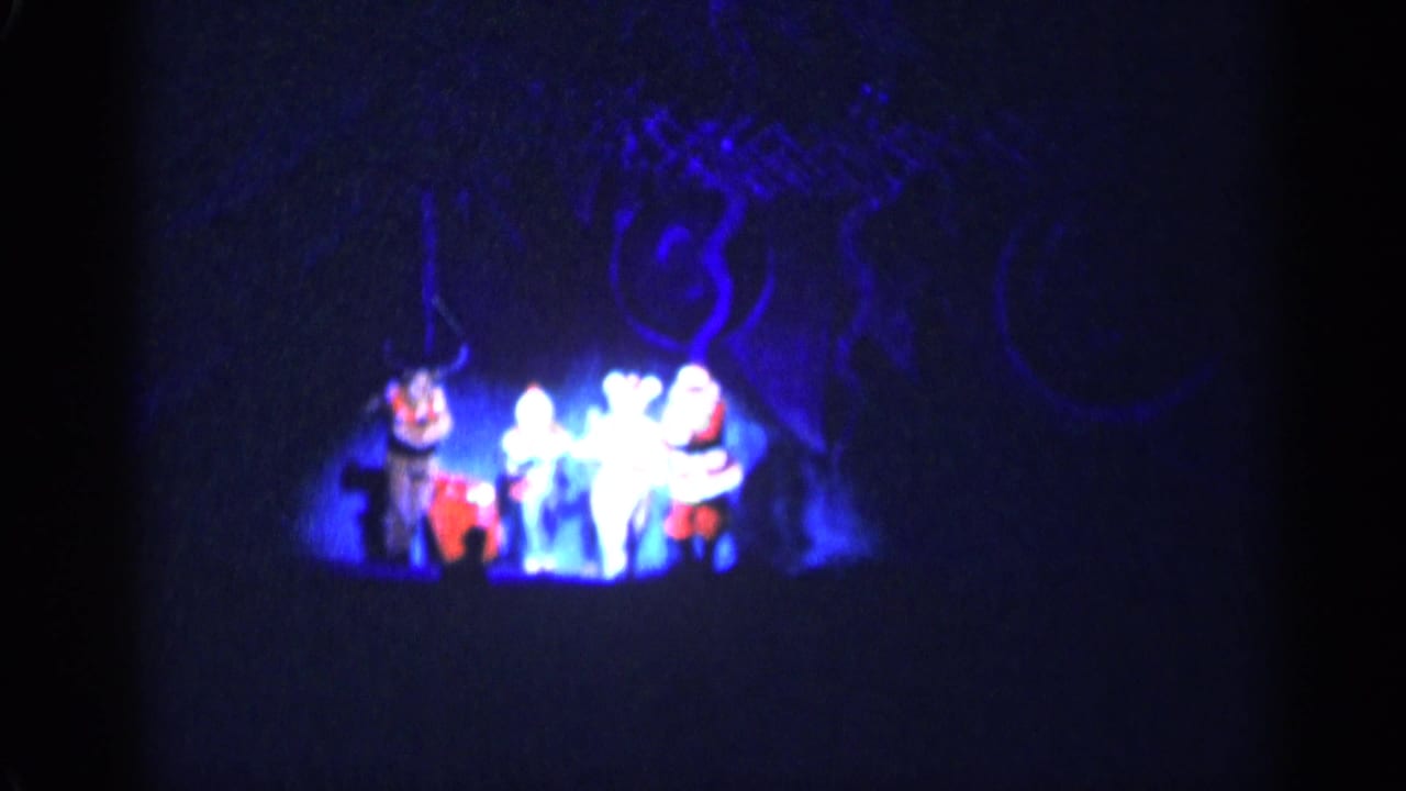 Four costumed performers dance on a dark stage under blue lighting.