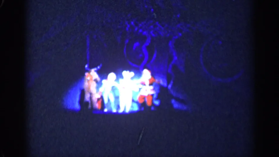 Blue-lit 1955 New York City home-movie frame of performers in Christmas-themed costumes moving across a dark stage.