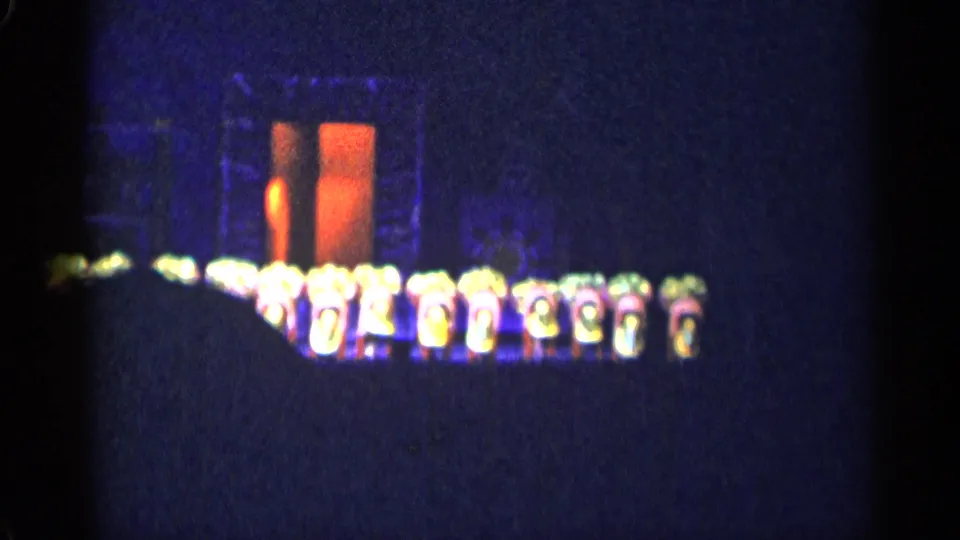 1955 New York City stage-performance frame with the troupe low across the stage in front of orange-lit set pieces.