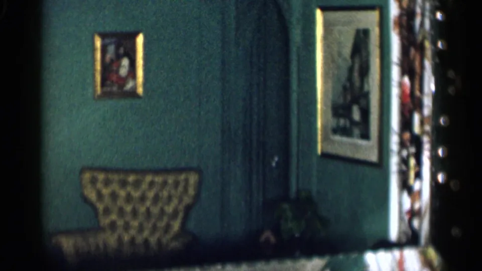 1955 home-movie view of a green wall with framed pictures and a patterned chair in a private New York City interior.