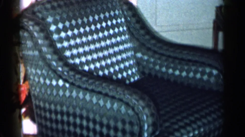 Close 1955 8mm view of a dark diamond-pattern armchair inside a New York City private home.