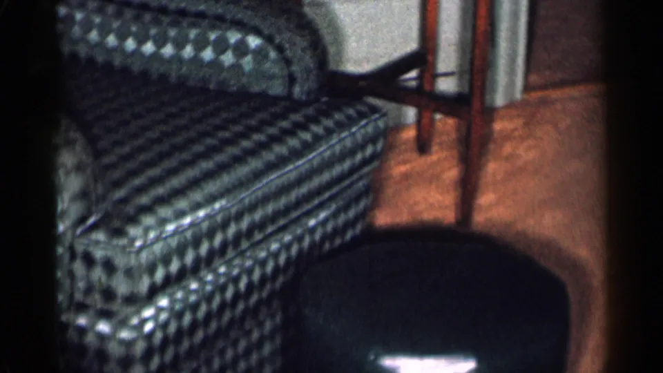1955 New York City interior frame showing the blue patterned armchair and a dark matching footstool on the floor nearby.