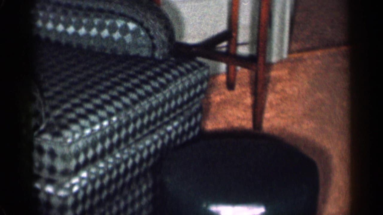 Green checkered armchair beside a dark leather ottoman in a living room.